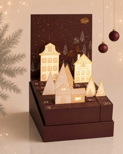 vomFASS Adventskalender 2026 aufgeklappt: Pop-up-Winterdorf mit Papierhäusern und Tannen über den nummerierten Türchen